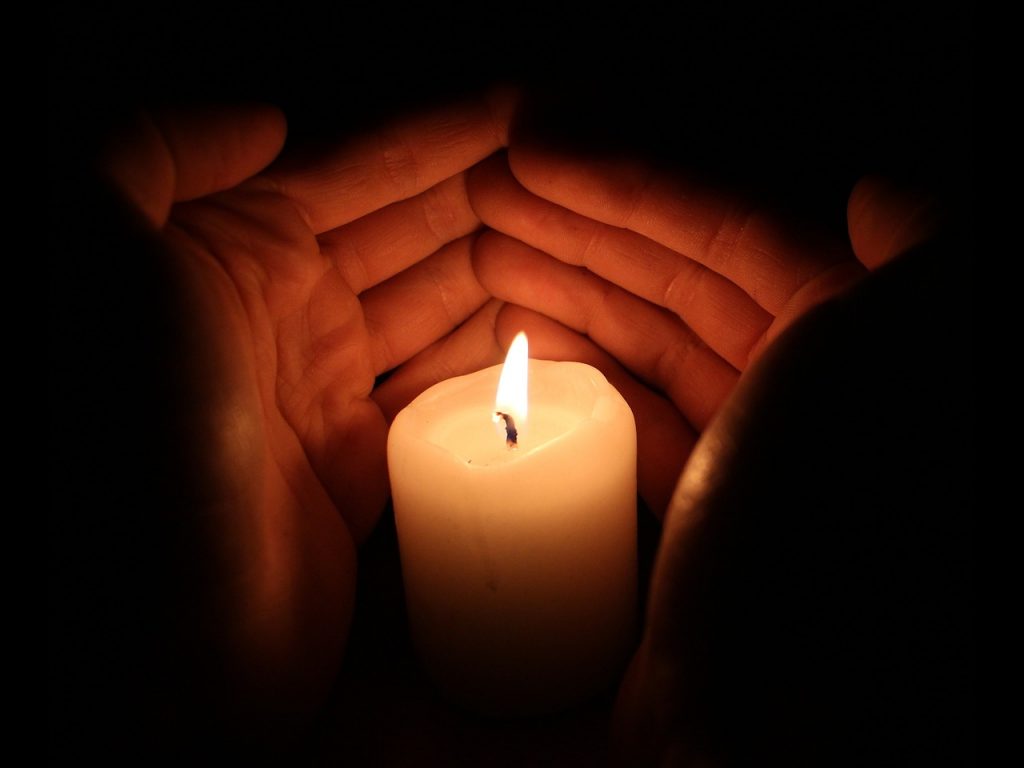 Two hands cradling a lit wax candle in the dark. Image by janwardenback on unsplash. https://pixabay.com/users/janwardenbach-3307393/
